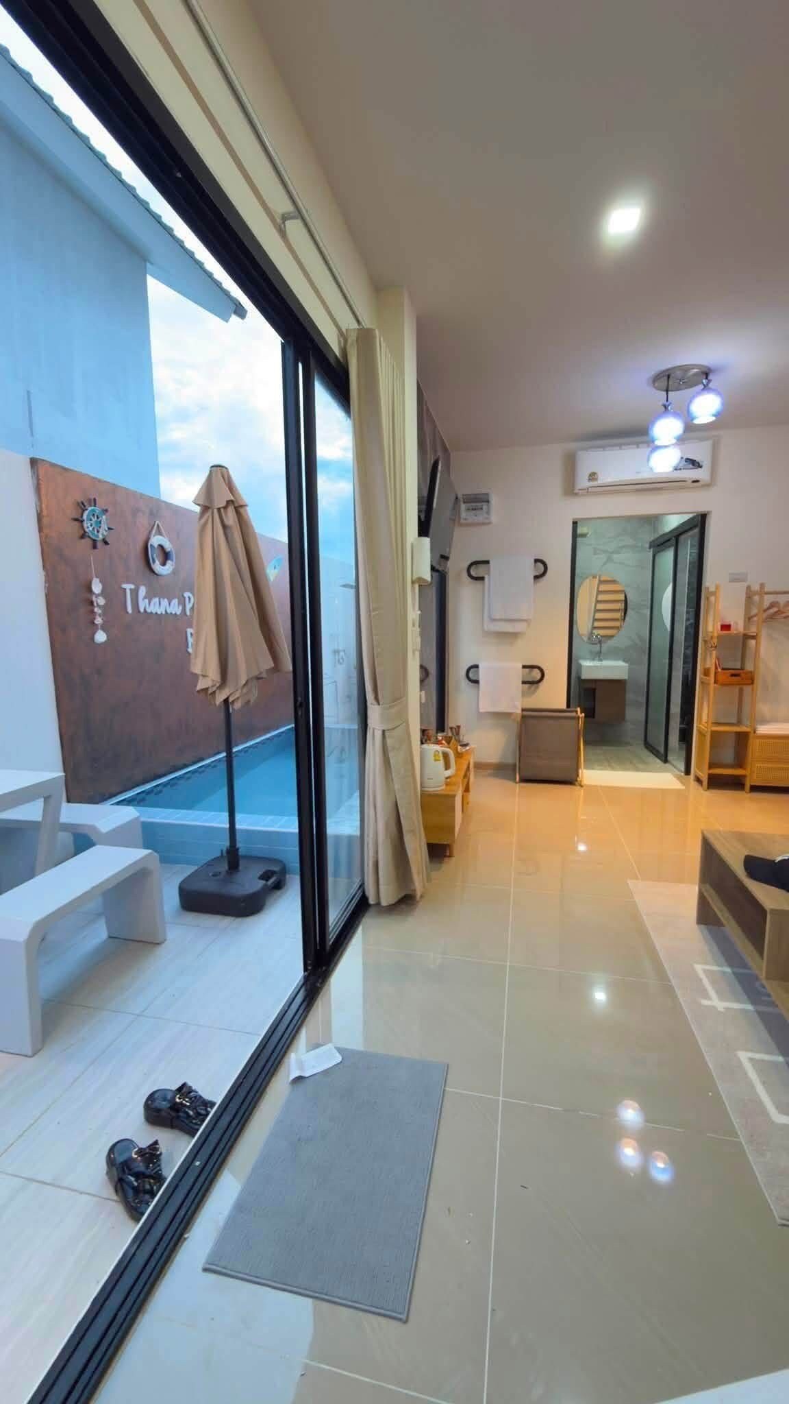 A modern hotel room with a large sliding glass door, a seating area with a bench and a table, and a view of the sky.