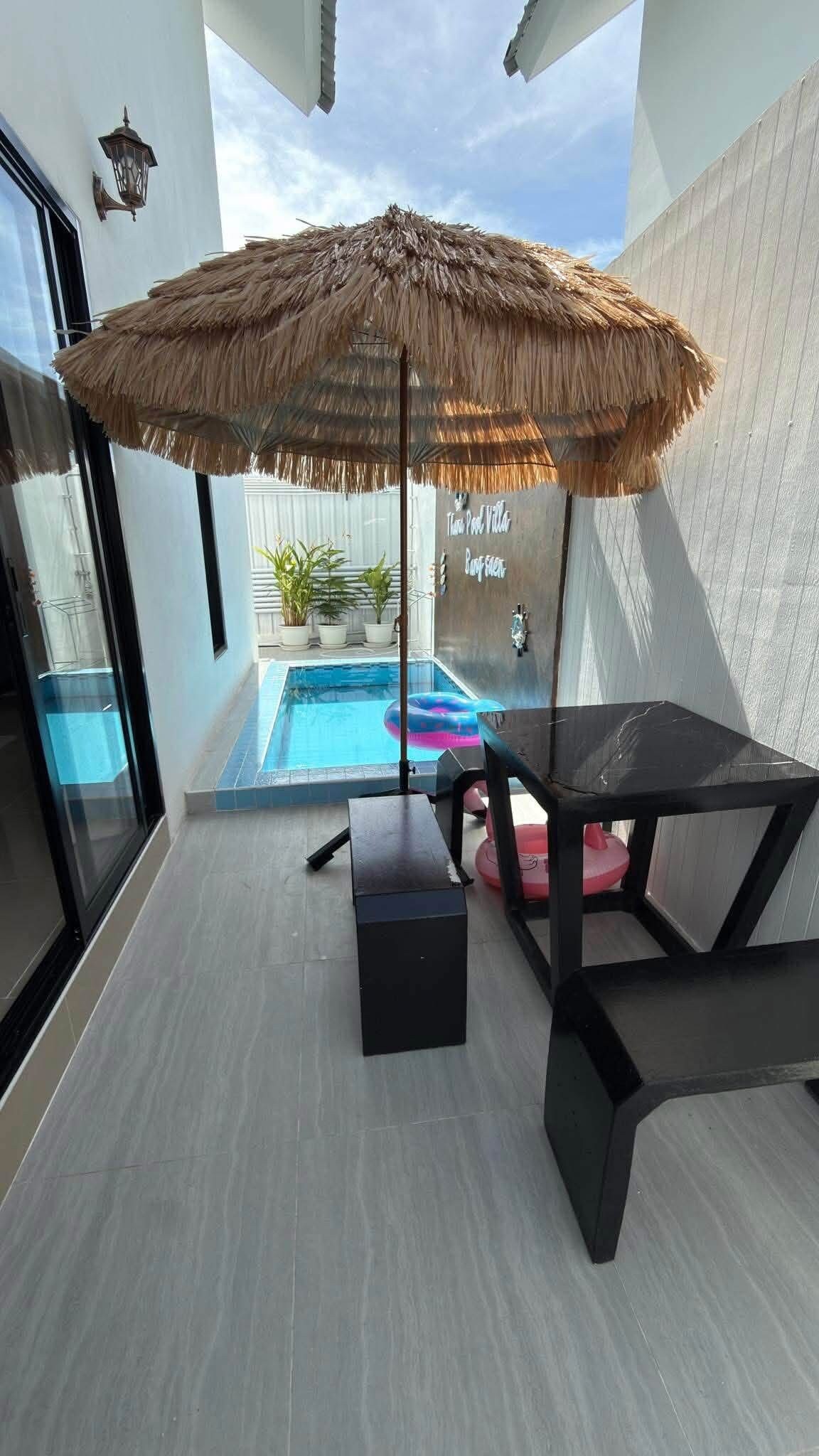 A poolside area with a thatched umbrella, a table, and chairs.