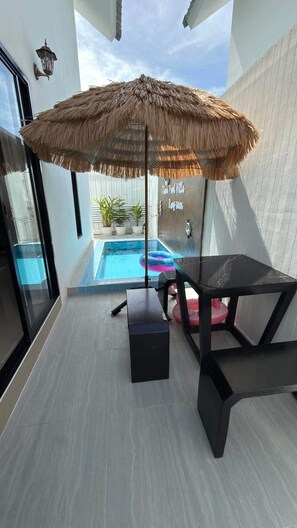 Un área junto a la piscina con una sombrilla de paja, una mesa y sillas.