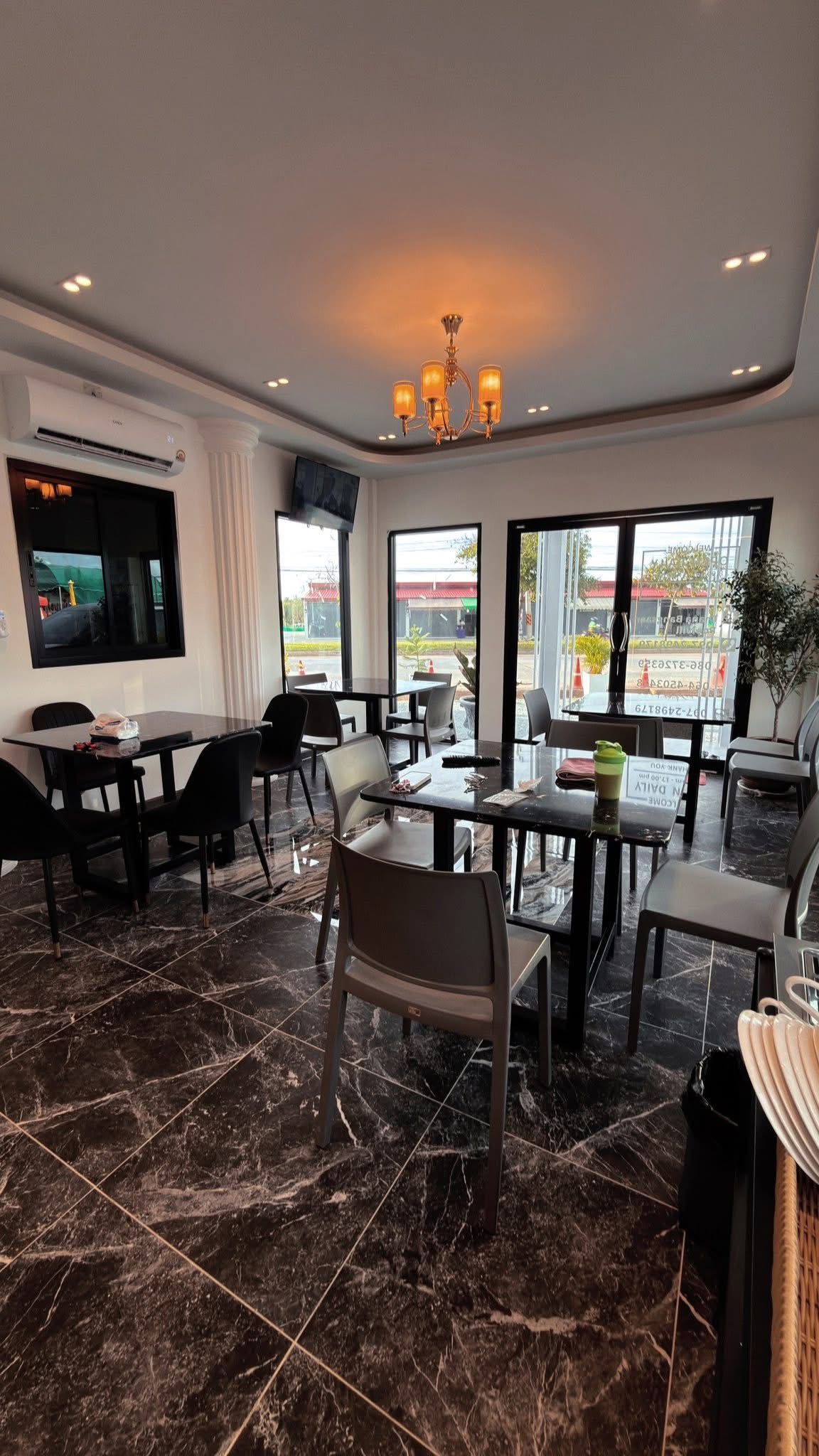 A modern dining area with marble flooring, black and grey chairs, and a chandelier.
