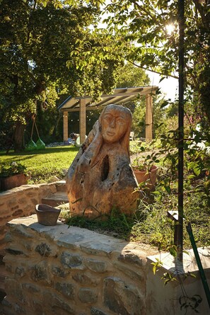 En stenskulptur i en trädgård, med en pergola som bakgrund.