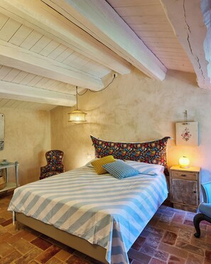 Ein Schlafzimmer mit Bett, Nachttisch, Sessel, Lampe und einer Pendelleuchte.