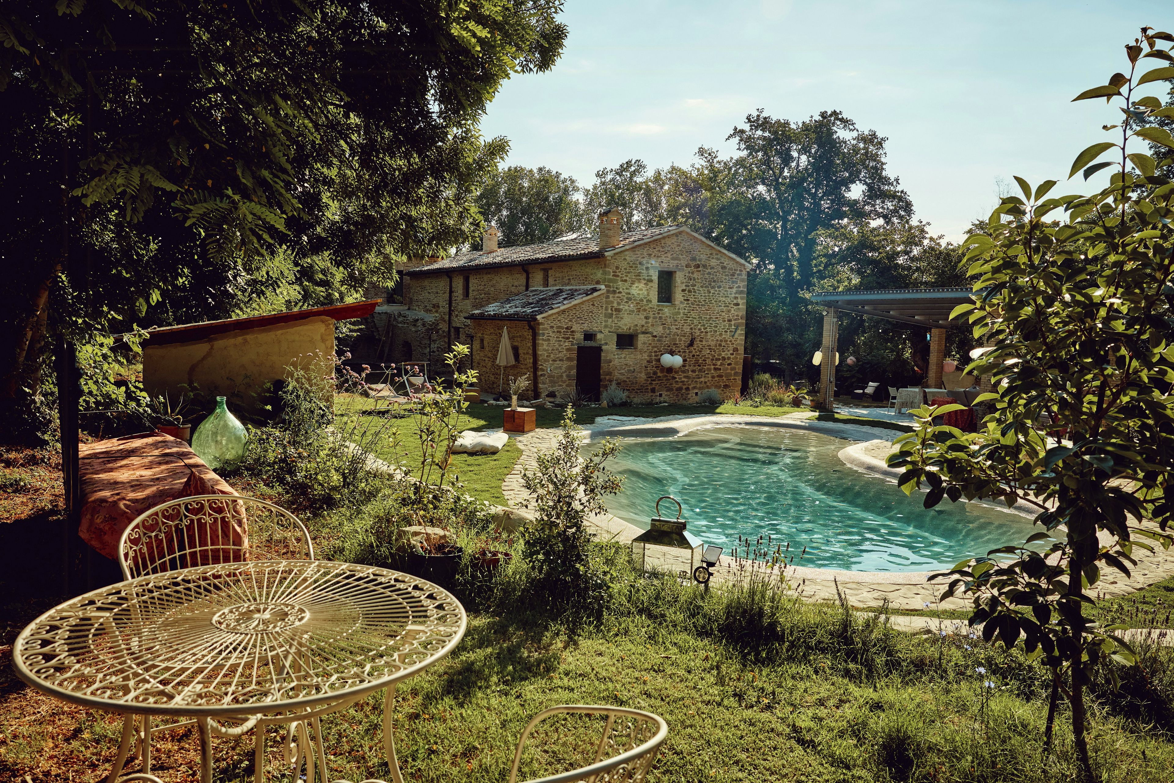 A stone building with a swimming pool, surrounded by greenery and a metal table.