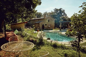 Edificio de piedra con piscina, rodeado de vegetación y una mesa metálica.