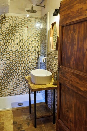 Ein Badezimmer mit einer Wand aus gemusterten Fliesen, einem runden Waschbecken auf einem Holzfuß und einer Dusche mit Glastür.