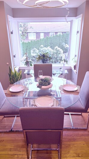 Un comedor con mesa de vidrio, sillas y vista a un jardín a través de un amplio ventanal.