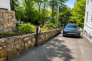 Una entrada de casa con un muro de piedra, un coche estacionado y una farola.