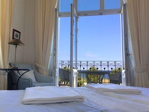 A hotel room with a bed, a chair, a table, and a view of the outside. - Villa Fortuna BY THE Sea, Apartment 5 (Heringsdorf)