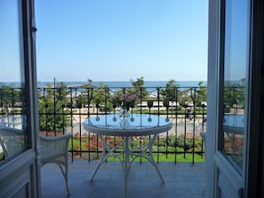 A balcony with a table and chairs, a view of the sea, and a garden with a fence. - Villa Fortuna BY THE Sea, Apartment 5 (Heringsdorf)