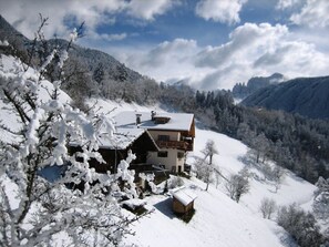Ein Chalet mit Holzbalkon, umgeben von schneebedeckten Bäumen und Bergen.