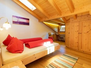Ein gemütliches Schlafzimmer im Loft-Stil mit Holzbalkendecke, einem Bett mit roten Kissen, einem Schreibtisch und einem Fenster.