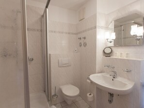Ein Badezimmer mit einer Duschkabine, einer Toilette, einem Waschbecken mit Spiegel und einem Toilettenpapierhalter.
