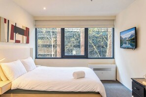 A bedroom with a large bed, a window with a view of trees, a radiator, and a painting on the wall. - CBD Studio by Vic Market | Gym, Wi-Fi & Free Tram (Melbourne)