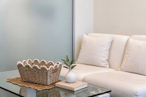 A modern living room with a glass coffee table, a woven basket, a book, and a potted plant. - CBD Studio by Vic Market | Gym, Wi-Fi & Free Tram (Melbourne)