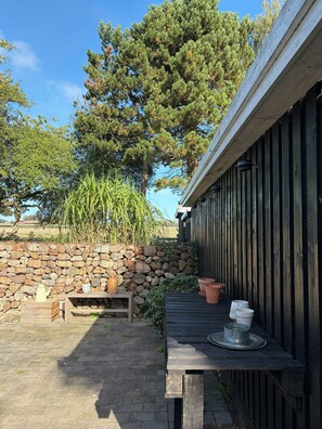 Eine Holzterrasse mit einer Steinsäule, einer Holzbank und einem Tisch mit einem Metalltopf und einem Glasbehälter.
