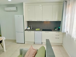 Cocina compacta equipada con refrigerador, lavavajillas y un lavamanos con grifo moderno.