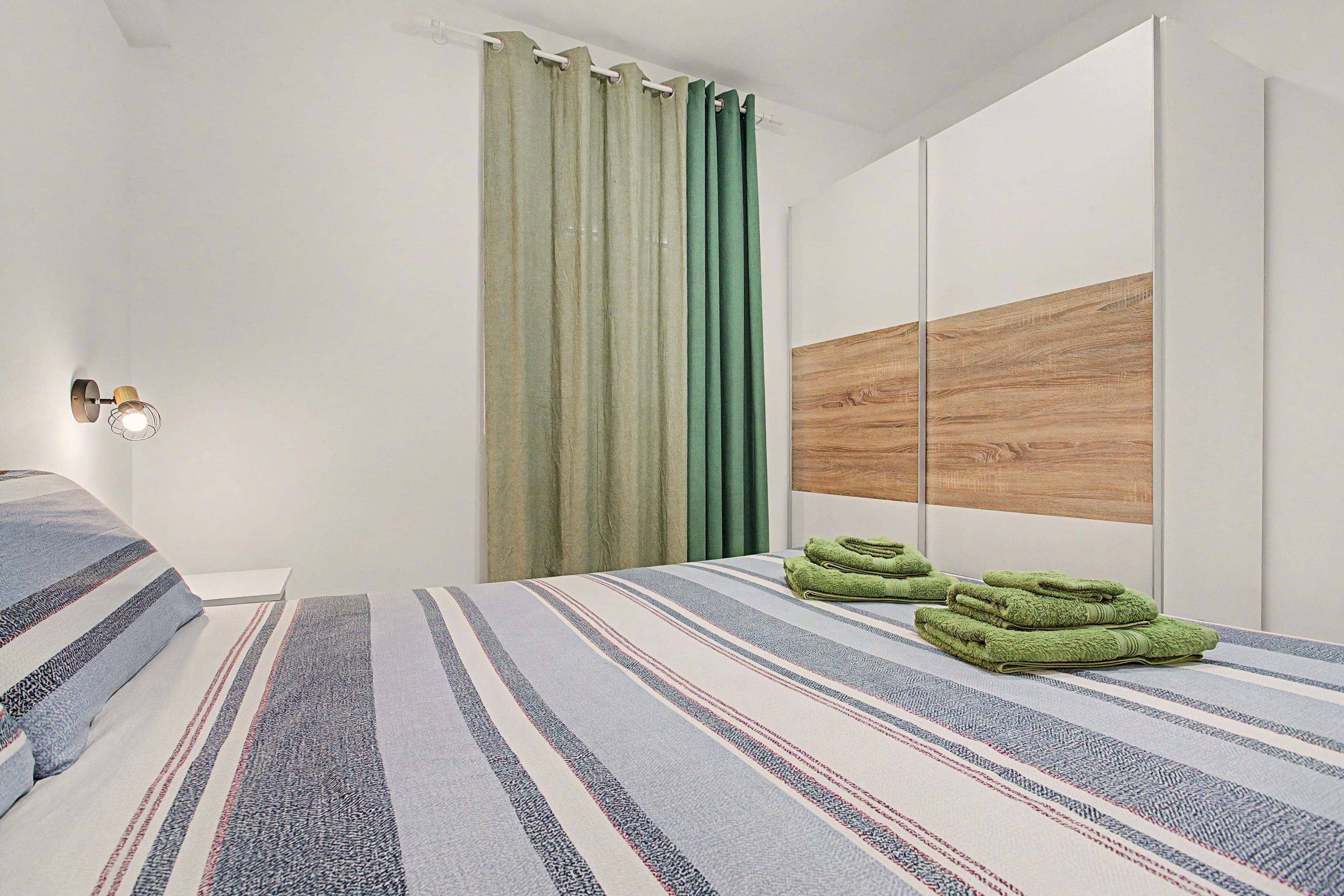 A modern bedroom with a bed, a wall-mounted light, a curtain, and a wooden panel.