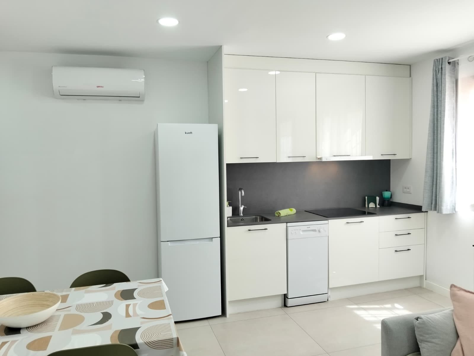 Una cucina moderna con mobili bianchi, lavastoviglie integrata e frigorifero.