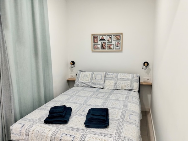 Una cama bien tendida con ropa de cama estampada, dos toallas dobladas, un marco de pared y lámparas de noche.
