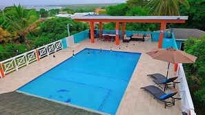 A rooftop swimming pool with a covered seating area, surrounded by greenery and a view of the city. - Beautiful Villa Views (Tobago)