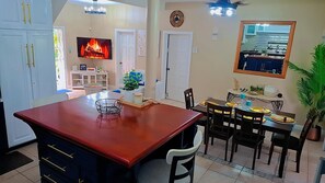 A dining area with a red table, chairs, and a small plant. There is a television mounted on the wall and a clock above the door. - Beautiful Villa Views (Tobago)