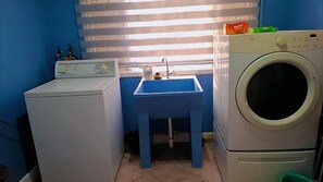A laundry room with a washing machine, a sink, and a window with blinds. - Beautiful Villa Views (Tobago)
