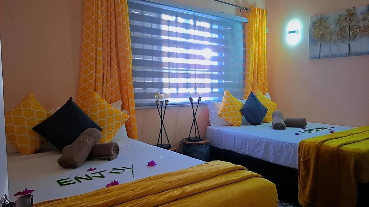 A hotel room with two beds, each with a yellow bedspread and pillows, a window with blinds, and a painting on the wall.
