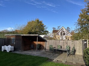 A backyard with a wooden shed, a table with chairs, and a fenced area. - Duinpan 22 Right by the sea (Kamperland)
