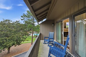 A balcony with two blue chairs, a glass door leading inside, and a view of a landscaped area with trees. - Relaxing Pinehurst Getaway - 2 Miles to The Cradle & 5 Minutes to The Village (Pinehurst)