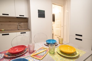 Une cuisine avec des meubles blancs, un plan de travail en bois et une table à manger dressée avec des assiettes colorées et un verre.