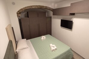 A hotel room with a bed, a wardrobe, a television mounted on the wall, and a small window. - One Bedroom apartment in the centre of Assisi (Assisi)