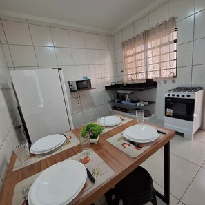 A compact kitchen with white tiled walls, a built-in oven, and a dining table set with plates and cutlery. - CASA 1111 FUNDO (São José do Rio Preto)