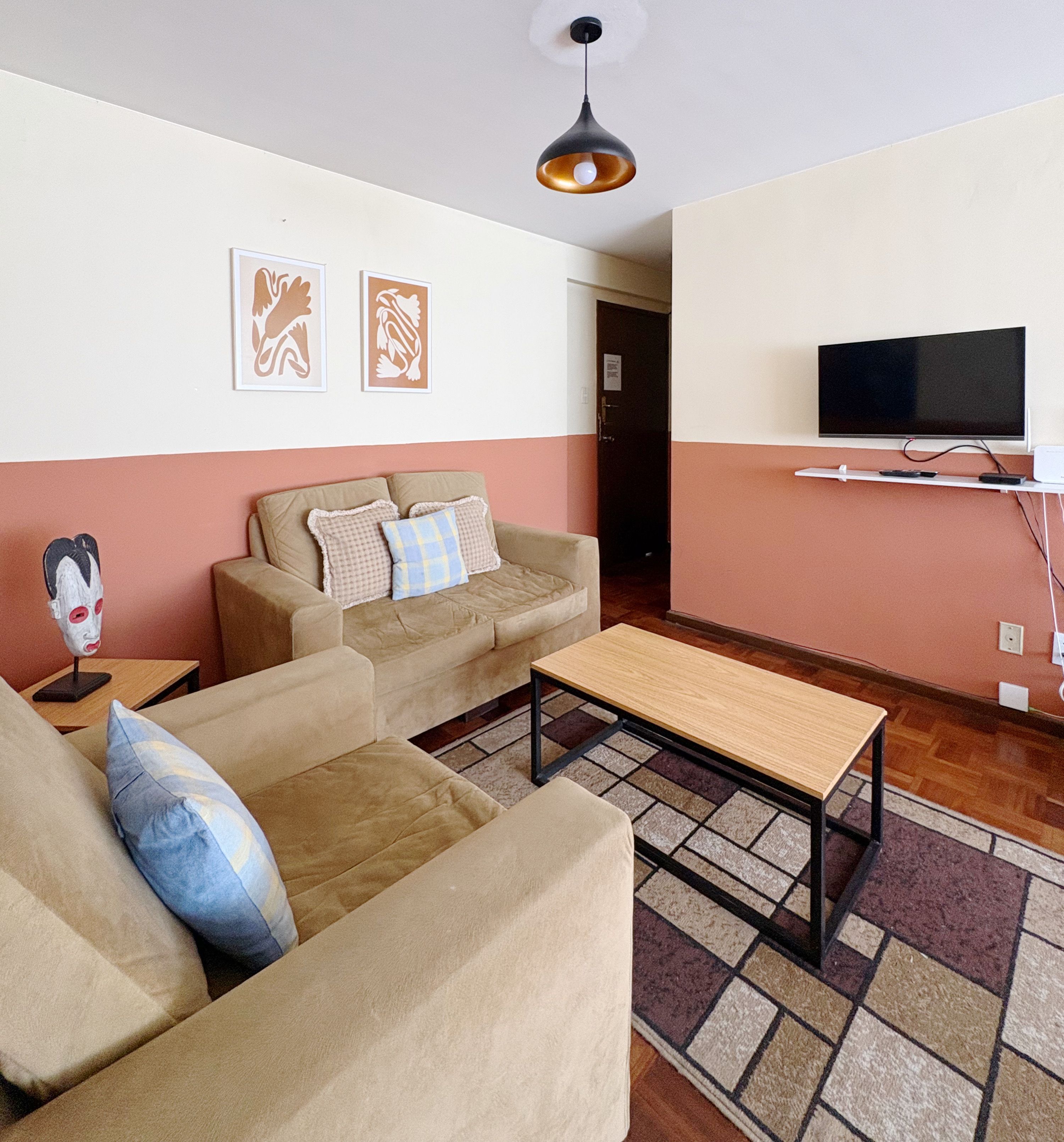 Una sala de estar con un juego de sofá, una mesa de centro, un televisor montado en la pared y una alfombra estampada en el suelo.