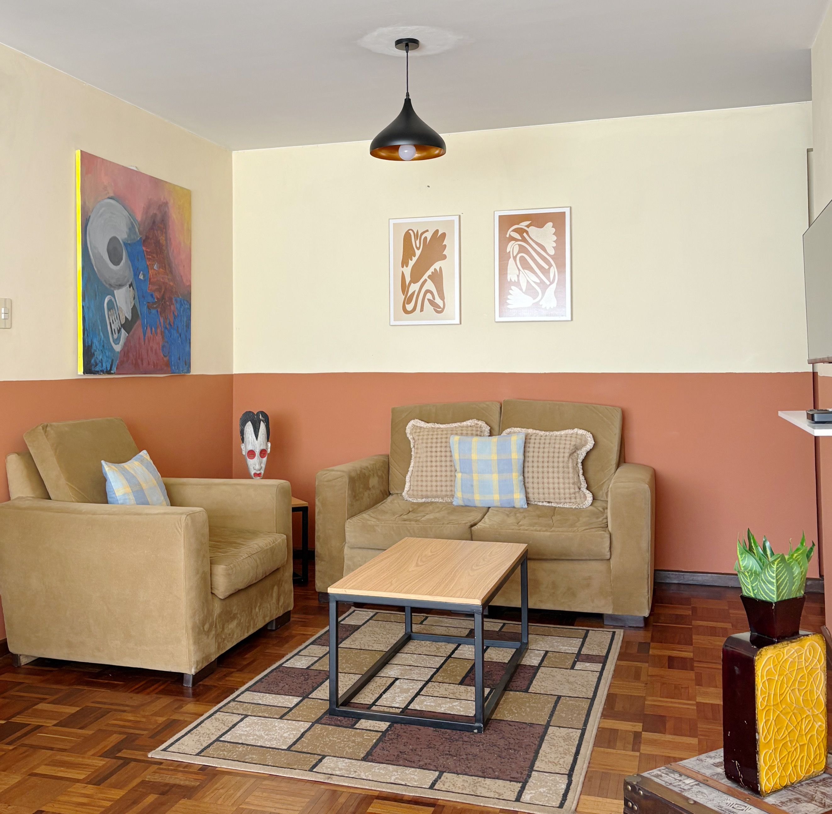 A living room with a sofa, armchair, coffee table, and artwork on the walls.