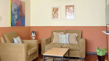 A living room with a sofa, armchair, coffee table, and artwork on the walls.