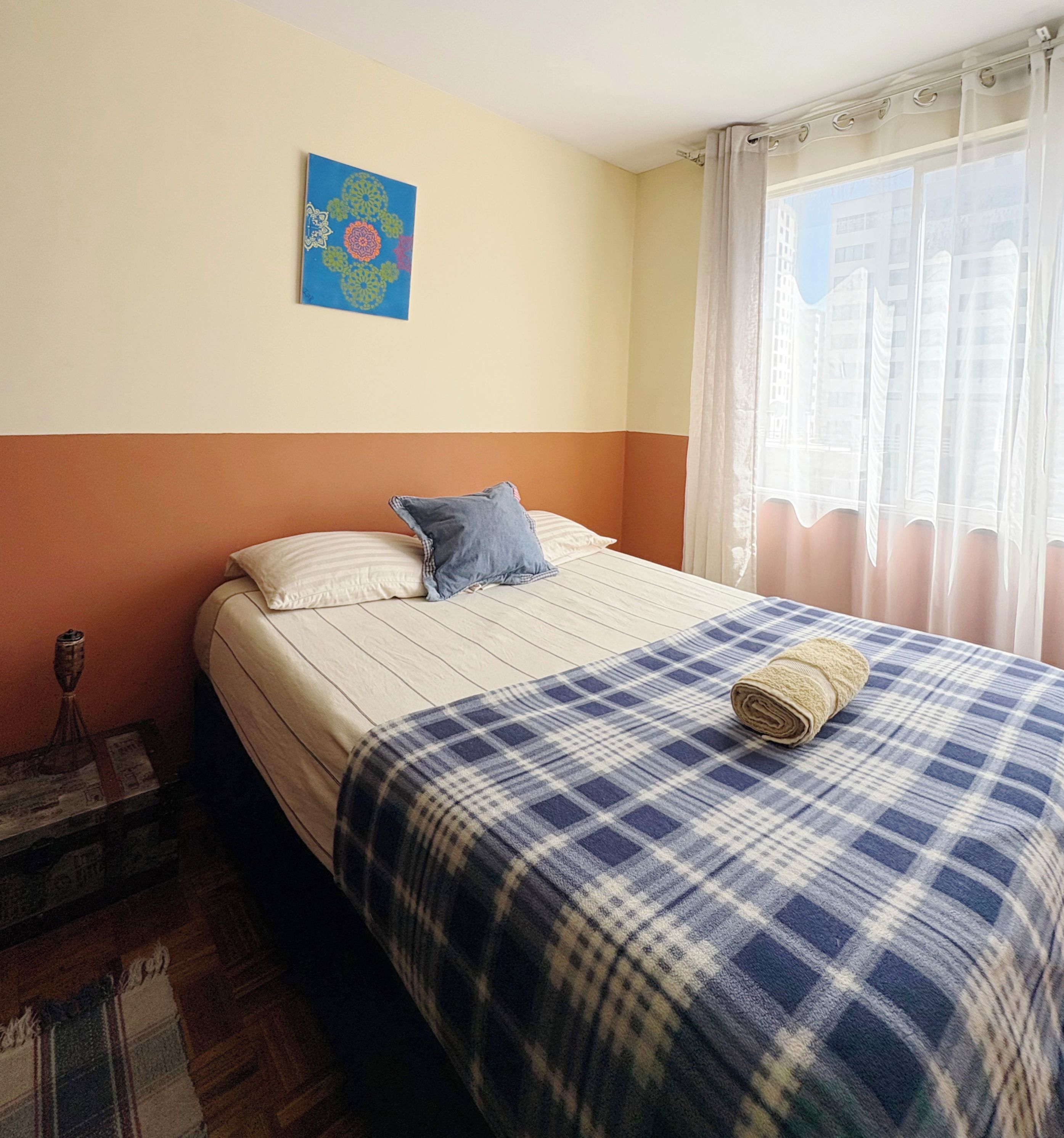 A bedroom with a bed, a pillow, a blanket, a wall painting, and a window with curtains.