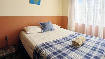 A bedroom with a bed, a pillow, a blanket, a wall painting, and a window with curtains.