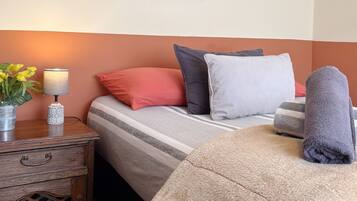 Habitación de hotel ordenada con cama, almohadas, lámpara de noche, una mesita con un jarrón de flores y un cuadro en la pared.
