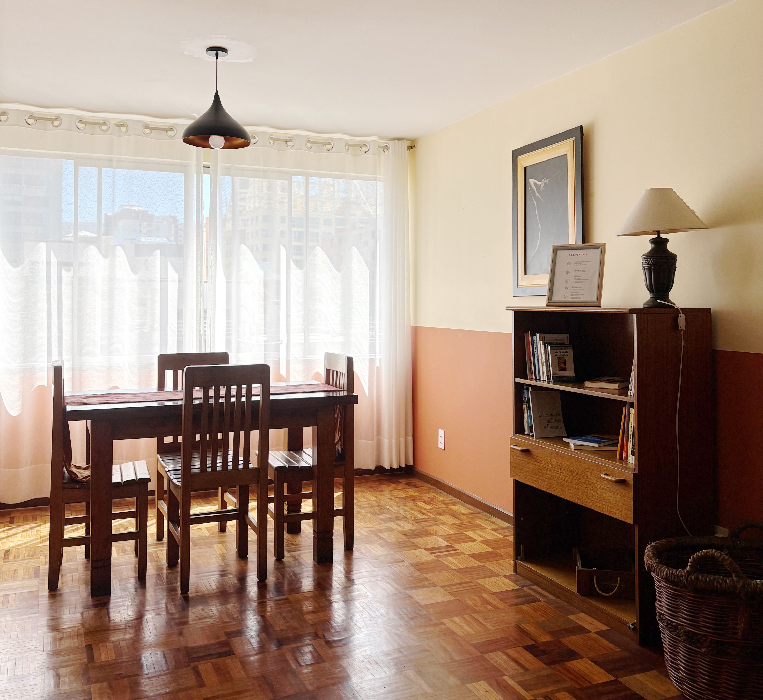 A dining area with a wooden table and chairs, a bookshelf, and a lamp.