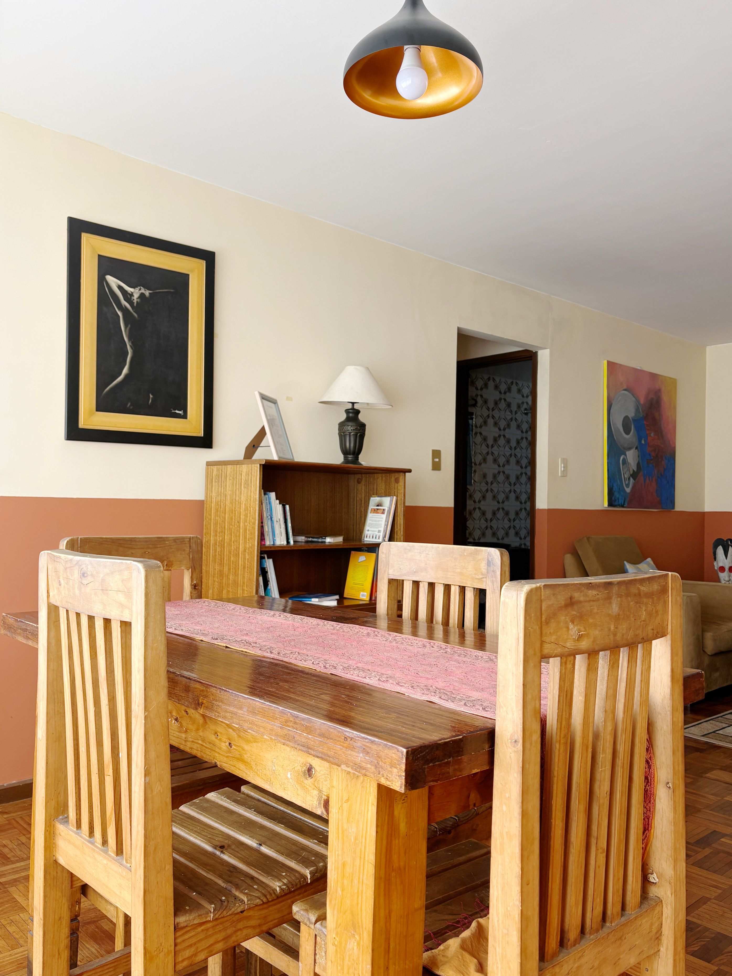 A dining area with a wooden table and chairs, a lamp, and artwork on the walls.