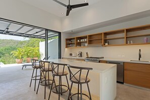 A modern kitchen with a bar area, built-in shelves, and a view of greenery outside. - Modern home overlooking golf course with private pool - minutes to the beach (Tangolunda)