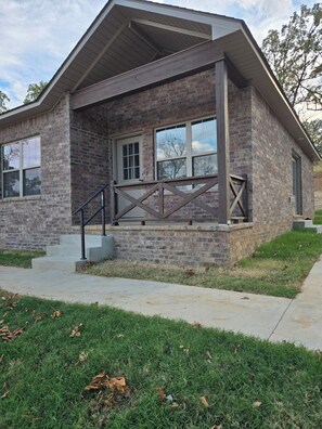 A two-story house with a brick exterior, a front porch with a railing, and a set of concrete steps leading to the entrance.