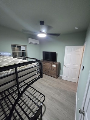 A bedroom with bunk beds, a dresser, a television, and a door.