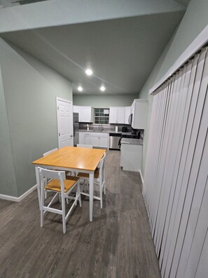 A compact kitchen with white cabinets, a wooden dining table, and a built-in oven.