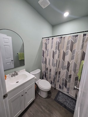Un baño con un lavamanos blanco, inodoro y cortina de ducha con estampado geométrico.