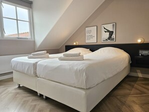 Ein Schlafzimmer mit zwei Betten, einem Fenster und einer Wand mit zwei gerahmten Bildern.