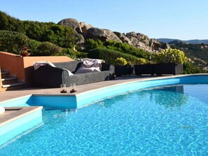 A swimming pool with a lounge area, steps leading into the pool, and a mountainous backdrop. - 1-bedroom Villa (Trinità d'Agultu e Vignola)