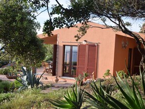 A building with a patio area, a dining table, and various potted plants. - 1-bedroom Villa (Trinità d'Agultu e Vignola)