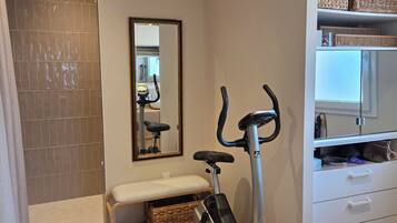 A modern bathroom with a shower, a bench, an exercise bike, and a storage cabinet.