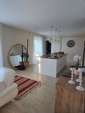 A modern living room with a white sofa, a wooden coffee table, and a kitchen area with a central island. - Single-family home with a private pool (Montélimar)